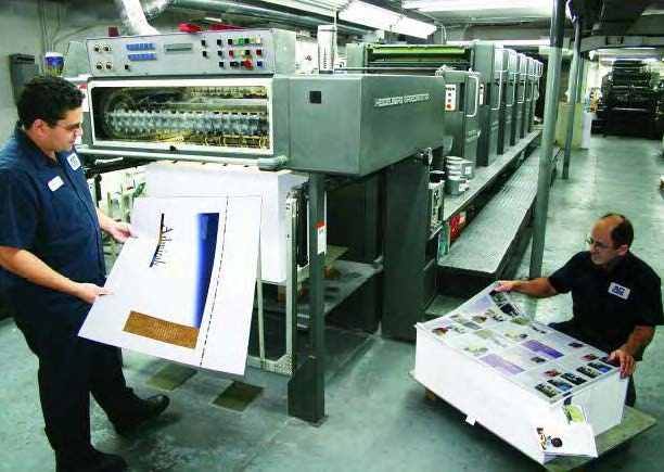 AC Graphics staff reviewing large color print proofs in front of commercial offset printing press in Miami